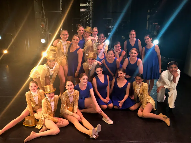 ETAP company members in gold and blue costumes pose together backstage on tour
